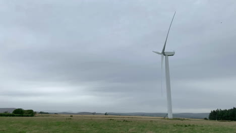 lado en la toma de un singular aerogenerador girando en un parque eólico de northumberland en un día nublado