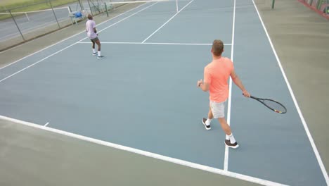 Two-diverse-male-friends-playing-doubles-returning-ball-on-outdoor-tennis-court-in-slow-motion