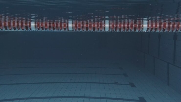 Ripresa subacquea laterale di una giovane nuotatrice con cuffia e occhialini che si tuffa in piscina 1