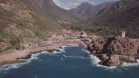 aerial footage of corsican city porto with its genoese tower in front of mountain scenery