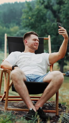 man taking a selfie in a wooden chair outdoors during a rain shower