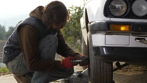 uomo inginocchiato che fissa la ruota dell'auto stringendo i dadi dei pneumatici con strumenti chiave