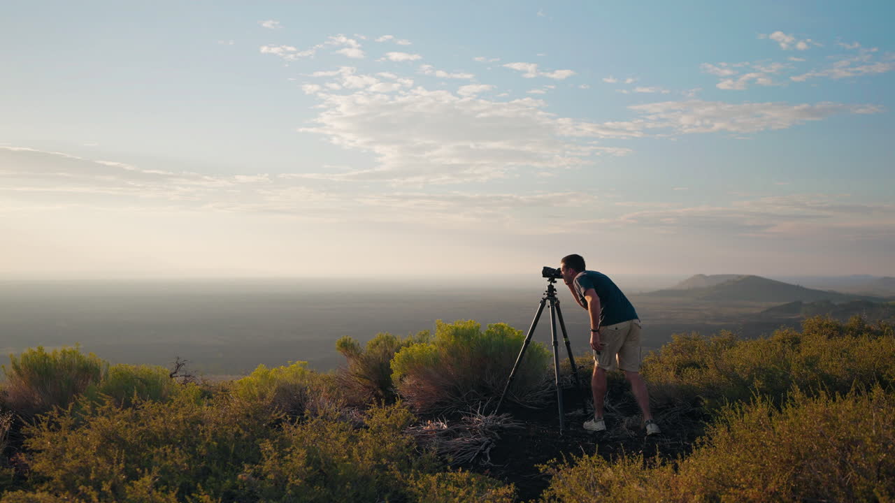 A man photographs a vast scenic landscape with a tripod at sunrise or sunset