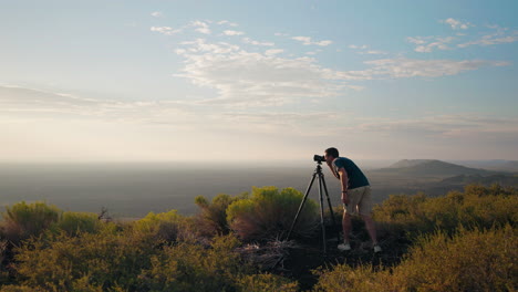 a man photographs a vast scenic landscape with a tripod at sunrise or sunset