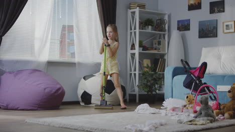 child pretending to sing while mopping a messy room