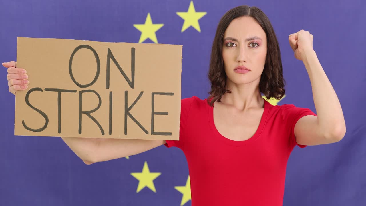 Kvinde står fast og holder skilt med ordene 'i strejke' ved et EU-flag.