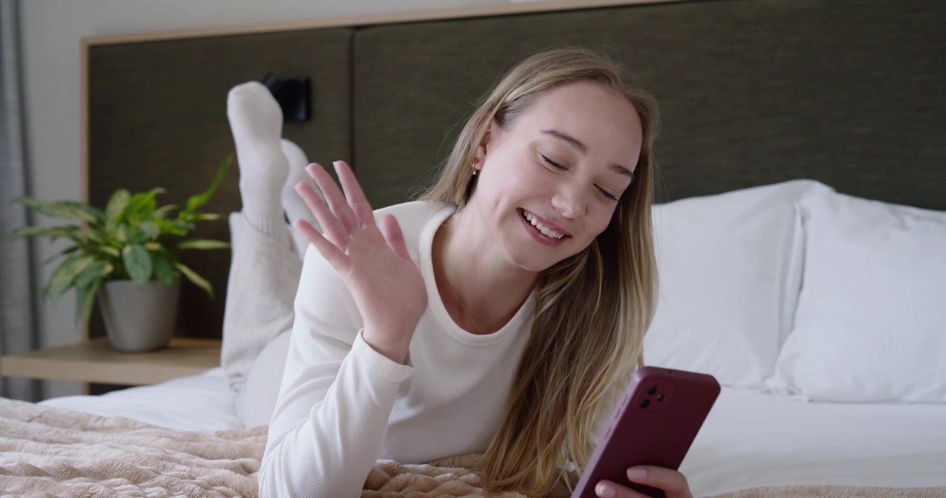 Donna sui vent'anni che riceve un messaggio, sdraiata a pancia in giù sul letto, che tiene un telefono rosso e tocca lo schermo.