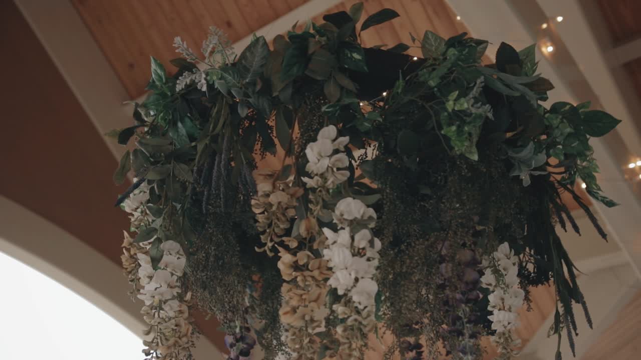 Ripresa ad arco di una ghirlanda floreale nuziale che ruota lentamente sotto un padiglione esterno durante una cerimonia di matrimonio
