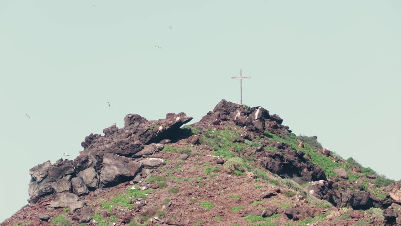 Gabbiani che volano intorno a una croce sulla cima di un'isola vulcanica