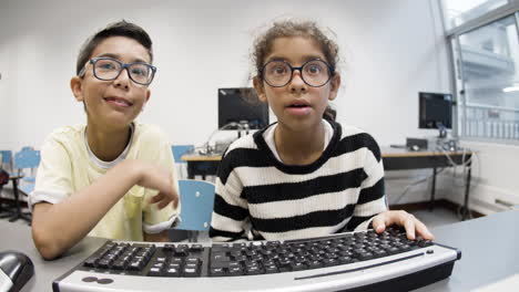 schoolkids sitting at table and typing on computer keyboard