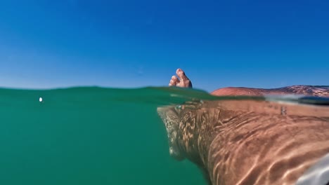 Fpv-Männlicher-Beine-Und-Füße,-Die-Sich-Beim-Schwimmen-Auf-Meerwasser-Mit-Horizont-Im-Hintergrund-Und-Blauem-Himmel-Darüber-Entspannen