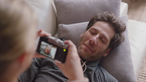 happy young couple taking photos together using camera having fun at home on sofa playfully enjoying romantic relationship photographing each other making faces