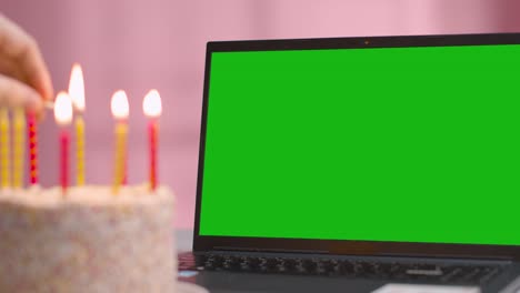 Green-Screen-Laptop-Mit-Geburtstagstorte,-Die-Mit-Brennenden-Kerzen-Im-Vordergrund-Bedeckt-Ist