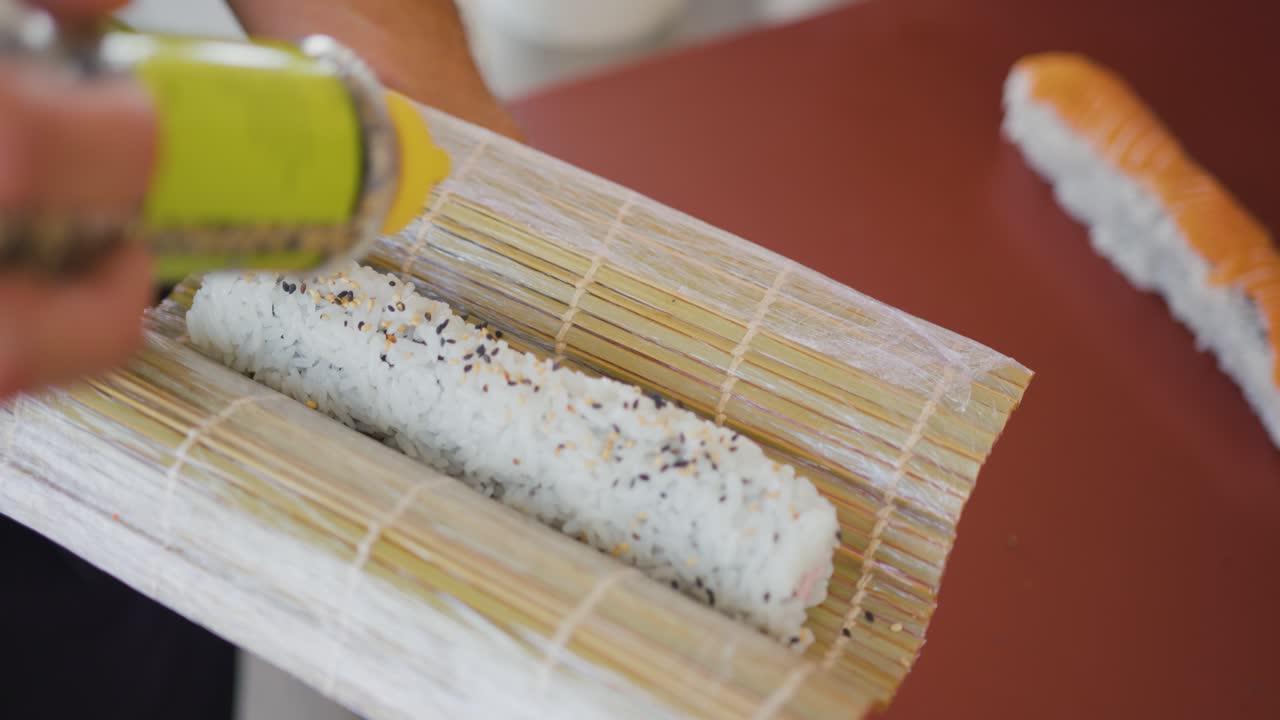 un chef profesional agrega semillas a un rollo de arroz, preparando un plato de sushi, cocina tradicional japonesa
