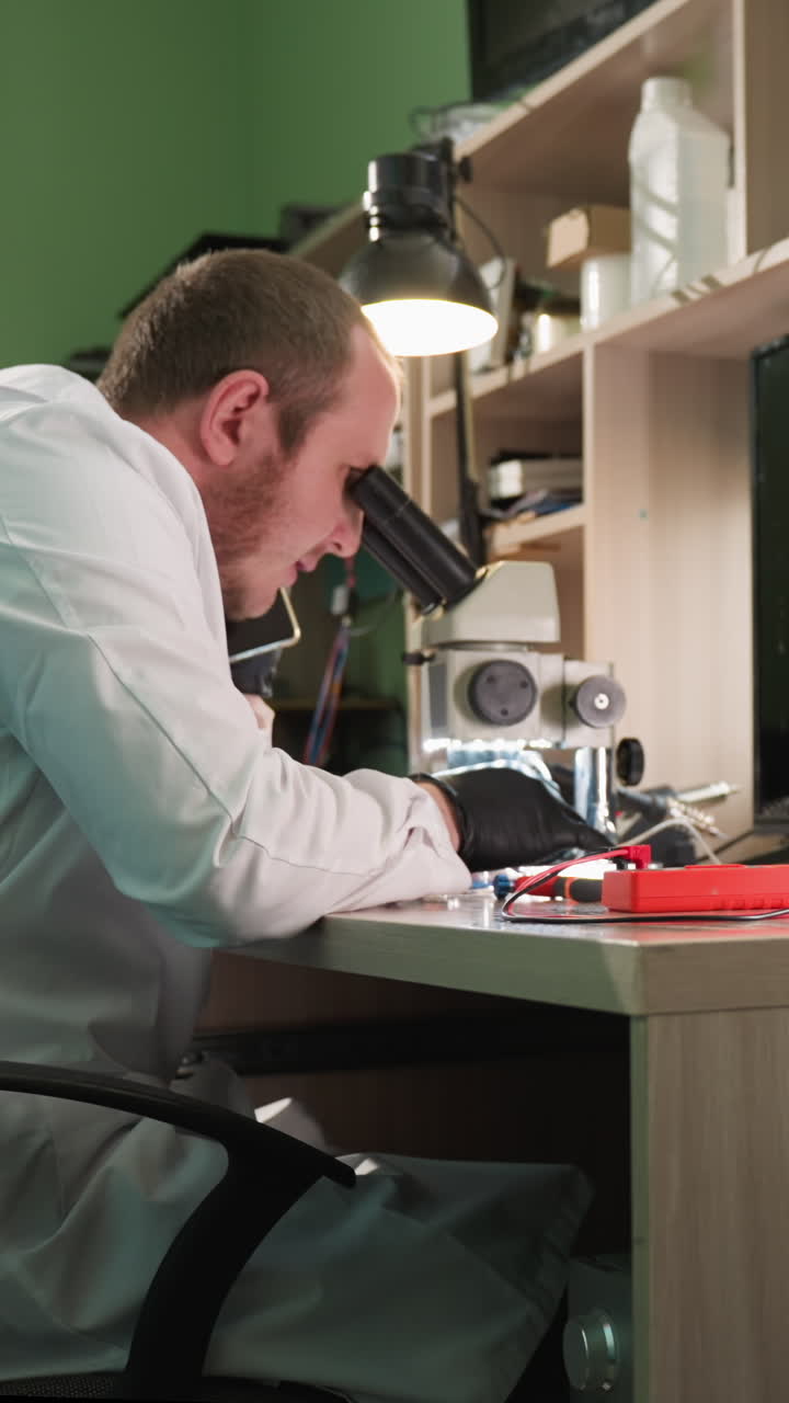 Una vista ravvicinata di uno scienziato in camice da laboratorio bianco che lavora diligentemente a una scrivania in un laboratorio, lo scienziato sta usando un microscopio e un telefono cellulare ed è circondato da vari strumenti