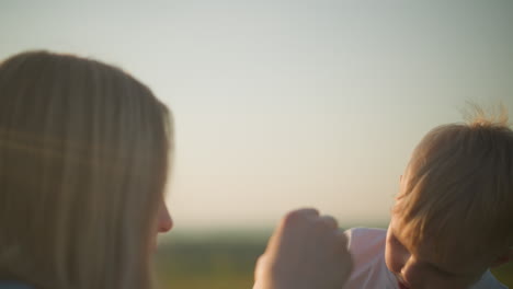 a heartwarming close-up of a young boy in a white shirt blowing bubbles with his mom. the setting sun bathes them in a warm, golden glow, enhancing the tender moment between mother and child