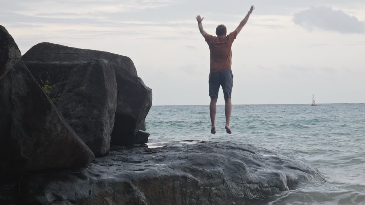 vista posterior de un hombre saltando sobre una roca frente al mar en la playa de dam trau en la isla de con dao, vietnam