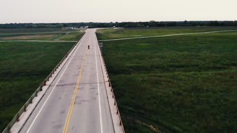 drone shot of single motorcycle riding across bridge