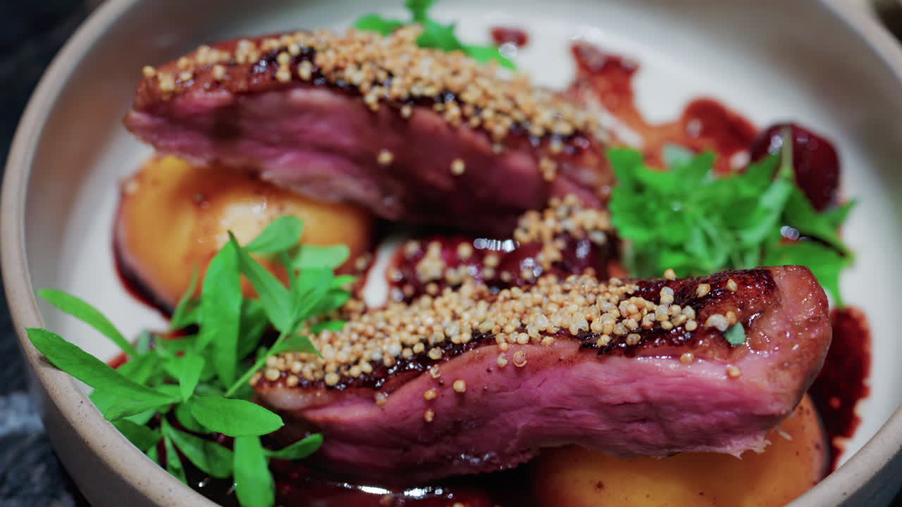 Close up of roasted duck breast plated with caramelized pear, crispy grains, and green herbs