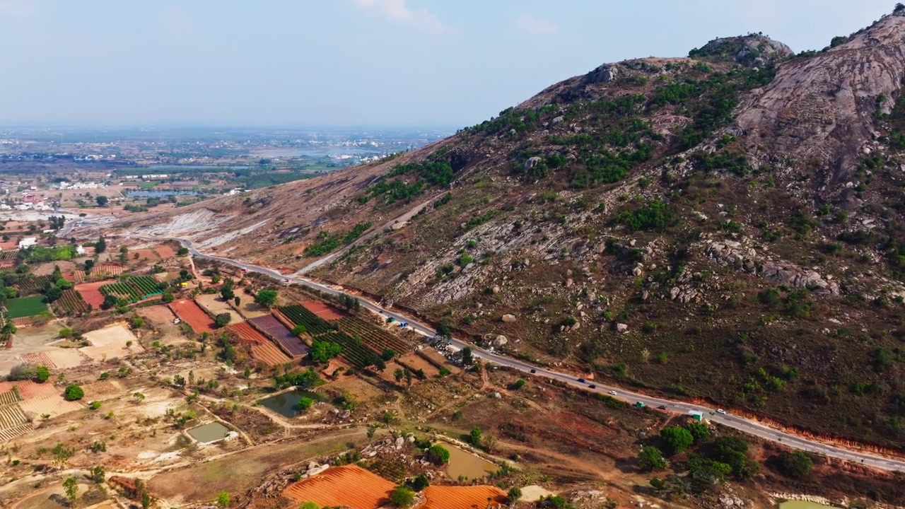 Campi coltivati con montagne e la strada Isha Adiyogi ad Avalagurki, Sonennahalli, Karnataka, India. Di giorno, ripresa in avvicinamento, ripresa con drone, 4K.