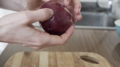 close shot as hands peeling of purple onion skin, preparation of vegetables in the kitchen