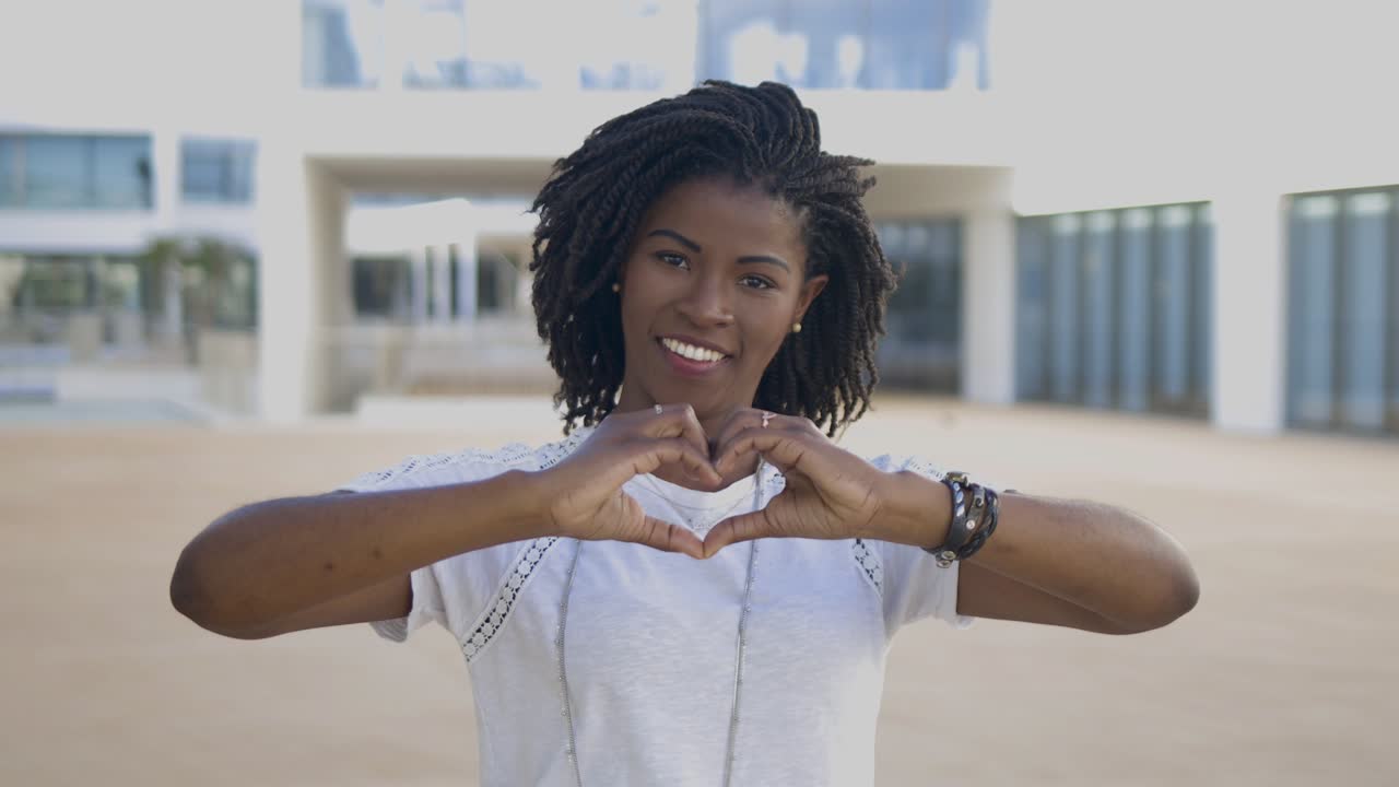 Donna afroamericana sorridente che forma un cuore con le mani.
