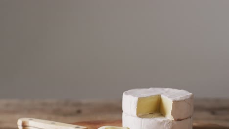 Video-close-up-of-soft-cheeses-and-knife-on-wooden-chopping-board,-with-copy-space