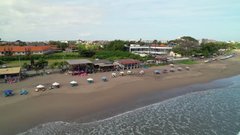 row of beach bars and cafes along winding batu belig beach coastline, parasols and deckchairs spread evenly in line, bali indonesia - aerial parallax