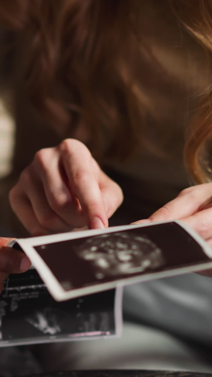 White woman shows baby on ultrasound pictures sitting with careful African-American husband in living room extreme close view slow motion