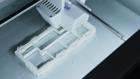 la cámara se desplaza sobre una impresora 3d que imprime un modelo de construcción de plástico en una empresa de arquitectura