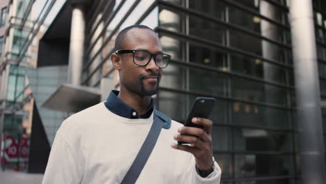 african american businessman walking through city using smart phone