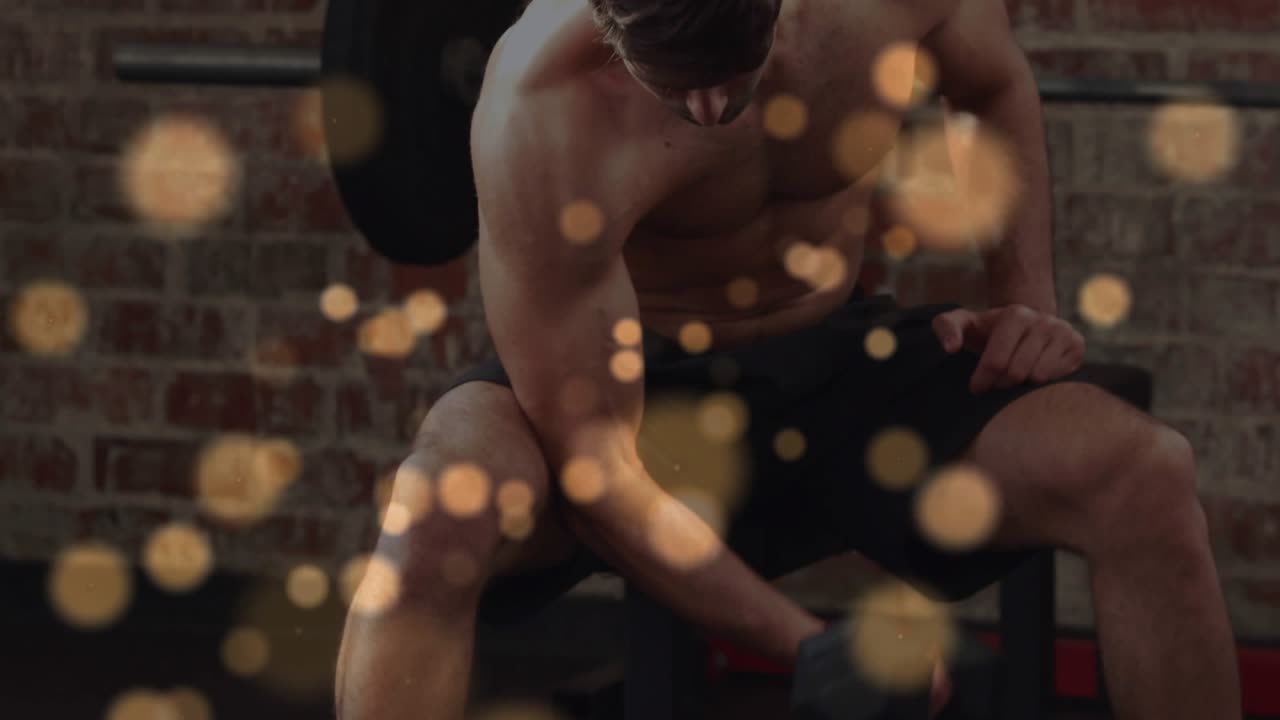 Man gripping hex dumbbell, doing curls in fitness studio, bokeh overlay flickering, celebrating set