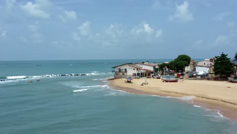 Dron-Aéreo-Giratorio-Amplio-Paisaje-De-La-Famosa-Ciudad-De-Playa-Tropical-De-Baia-Formosa-En-El-Estado-De-Rio-Grande-Do-Norte,-Brasil-Con-Barcos-De-Pesca,-Casas-Costeras,-Olas-Pequeñas-Y-Surfistas