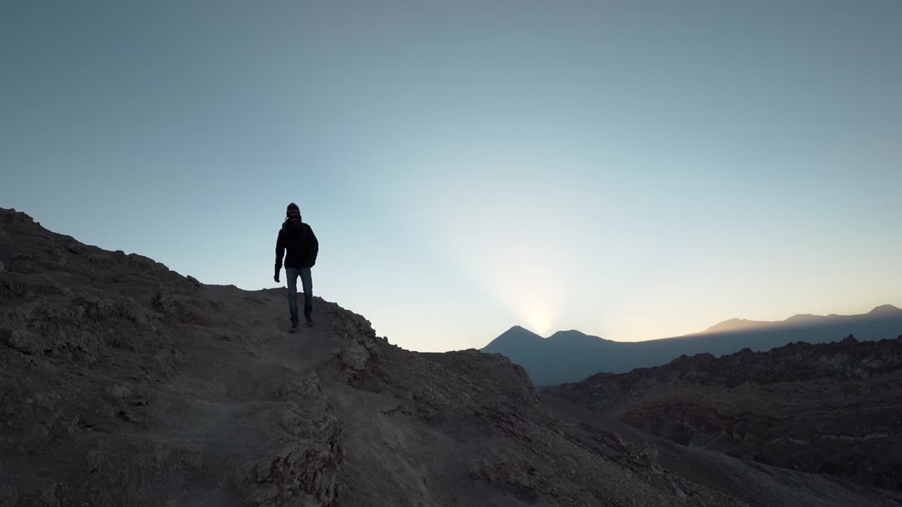 silueta de excursionista caminando por una montaña en el desierto al amanecer con volcanes en el fondo