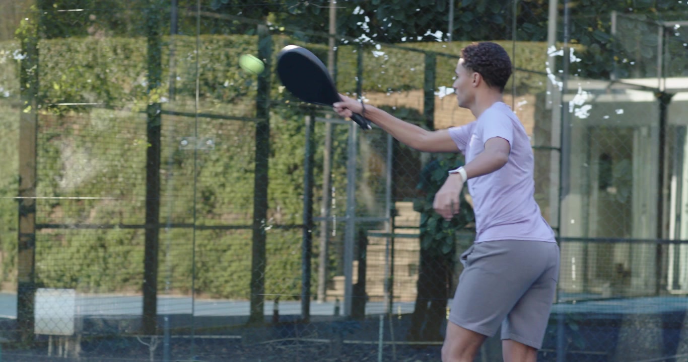 Diverse men tracking yellow ball, rallying, hitting return with paddle on glass court, copy space