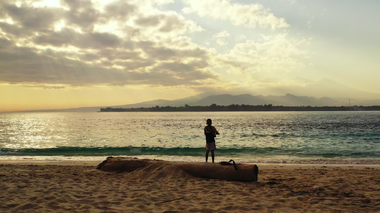호주의 아름다운 해변에서 멀리 떨어진 산 너머로 석양을 배경으로 낚시하는 청년