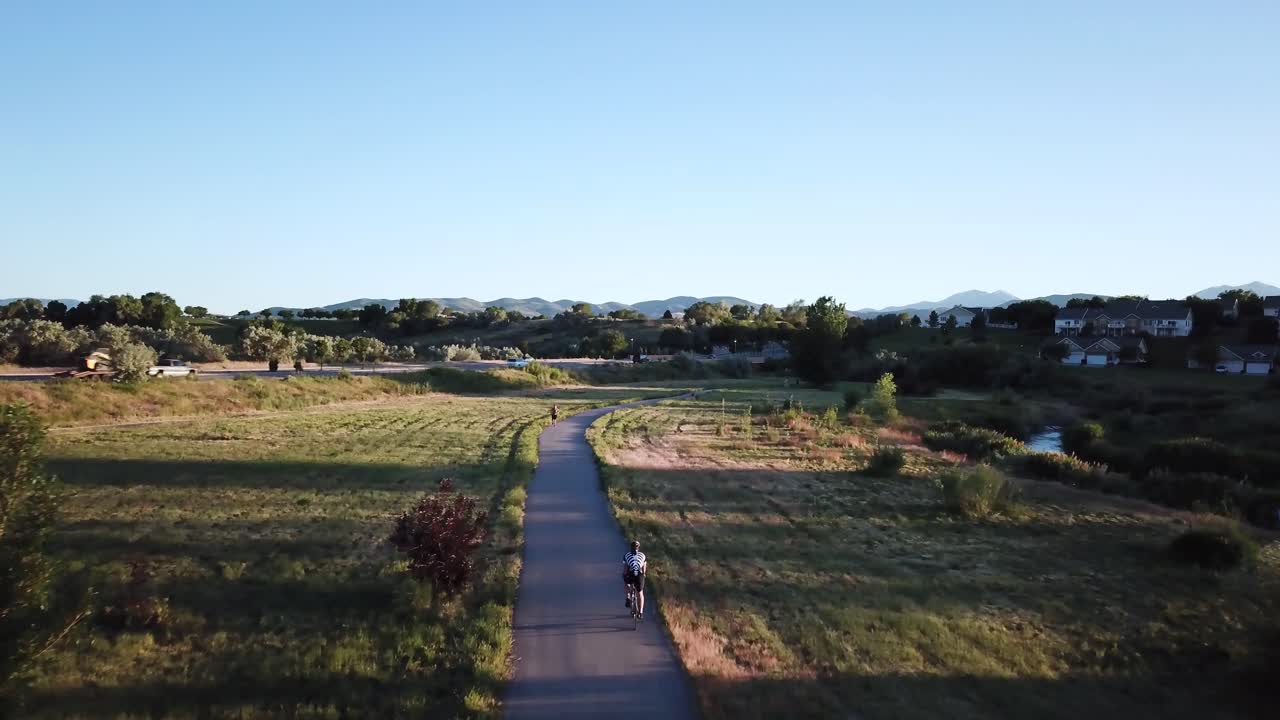 강과 바쁜 도로 옆의 자전거 도로를 따라 자전거를 타는 자전거 타는 사람을 따라 드론 샷