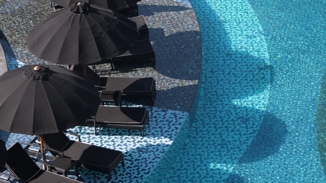 Outdoor Swimming Pool With Black Parasols And Sun Loungers At Hotel Resort In Bali, Indonesia. high angle, static shot
