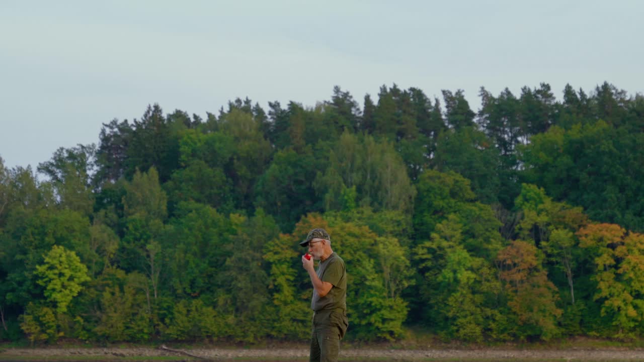 Senior men taking a bite into a red apple. Eating outdoors with verdant forest in the background.