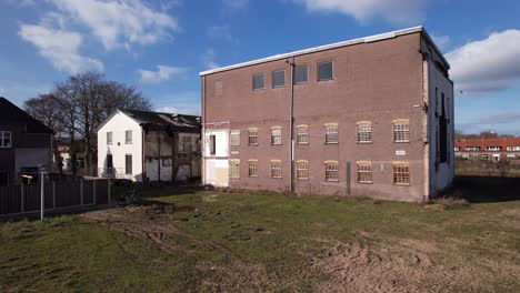 Low-closeup-aerial-pan-around-former-youth-prison-facility,-now-abandoned-waiting-for-demolition-and-refurbishment-of-the-moated-plot-field-in-a-residential-neighbourhood-of-Zutphen,-The-Netherlands