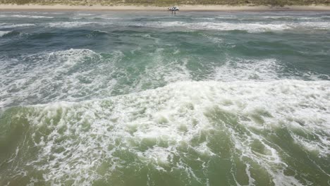 the waves from the gulf of mexico break onto the beach in port aransas, texas while a truck full of people enjoy sandy shores