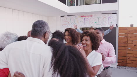 Family-running-to-welcome-grandparents-outside-their-home-for-a-surprise-party,-over-shoulder-view