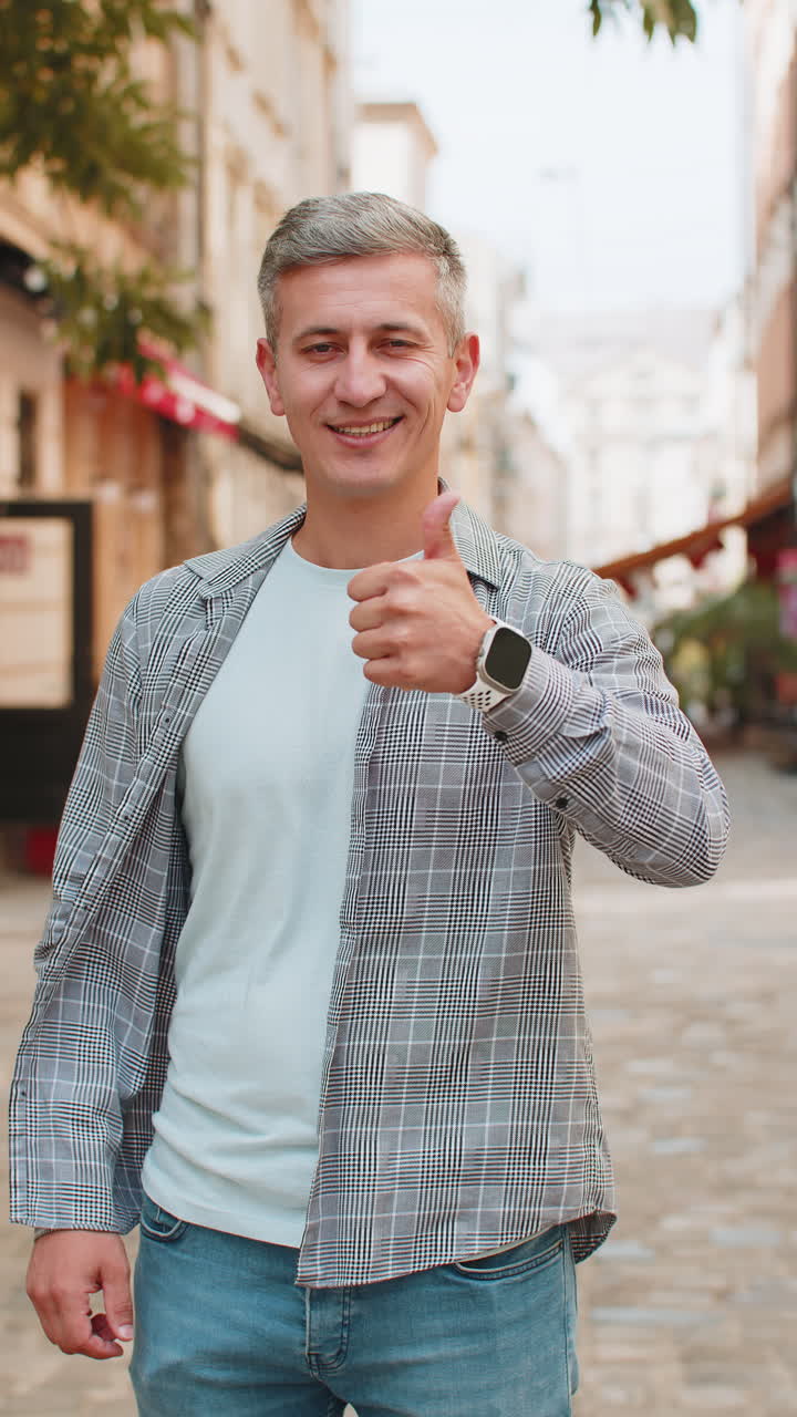 Happy mature man showing thumbs up agrees giving positive reply recommends good idea on city street