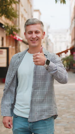 happy mature man showing thumbs up agrees giving positive reply recommends good idea on city street