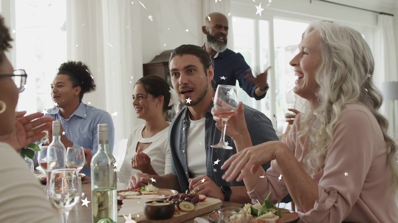 Convidado masculino iniciando um brinde à mesa, convidados aplaudindo e celebrando, com brilhos de estrela sobre uma tábua de vinhos.