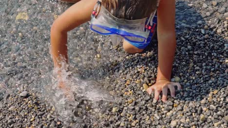 cerca de un niño caucásico cavando guijarros en el mar, tratando de crear una zanja a cámara lenta