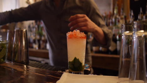el cantinero agrega jarabe, menta, pajitas a queen&#39;s park swizzle, cóctel mojito en el bar