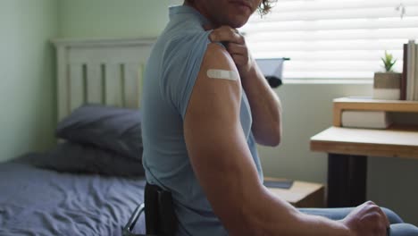 midsection of caucasian disabled man in wheelchair showing bandage on arm after covid vaccination