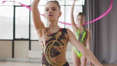 portrait of two young girls in leotard practising rhythmic gymnastics with a ribbon during a rehearsal in a studio