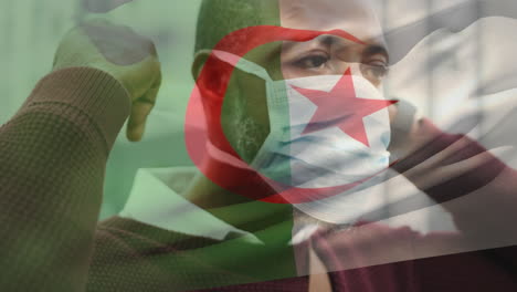 animation of flag of algeria waving over man wearing face mask during covid 19 pandemic